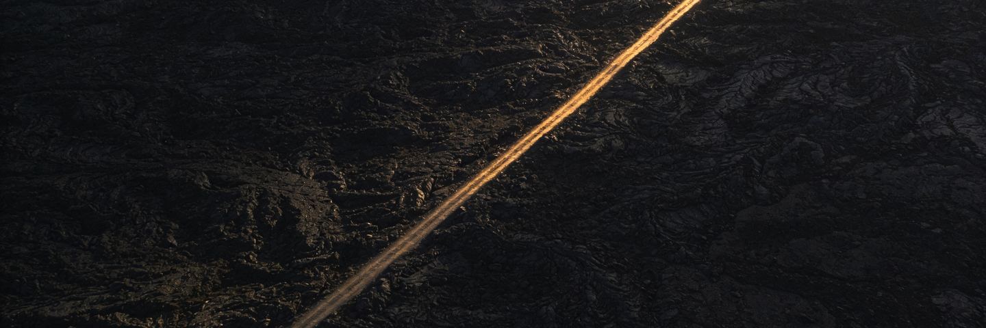 Aerial view of a single lit track crossing dark open ground